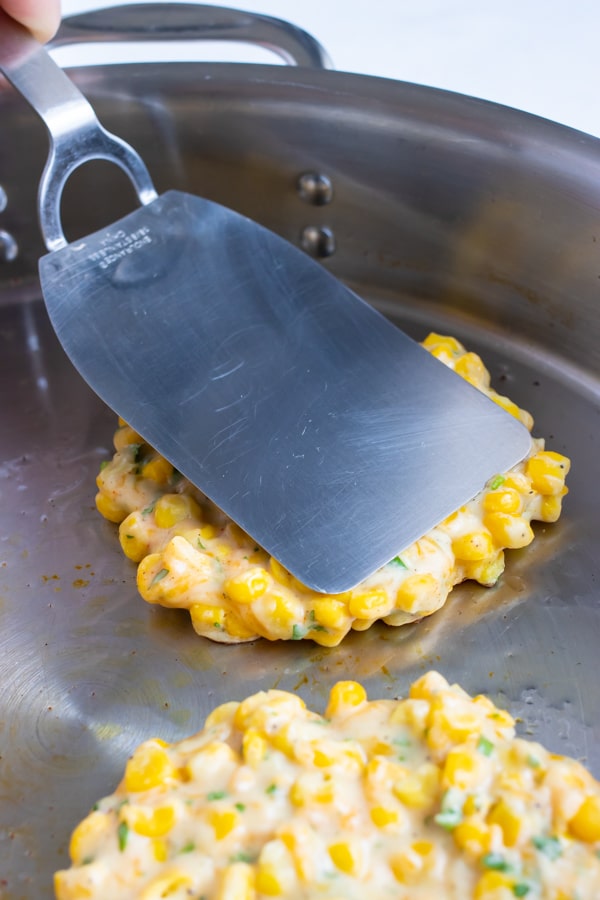 Corn fritters being fried in a skillet.