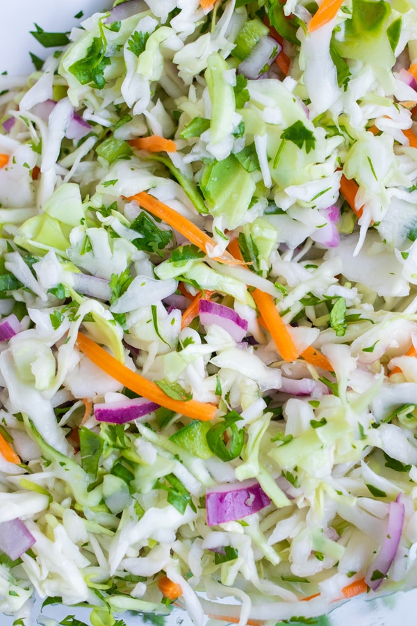 Taco slaw is made with shredded cabbage, red onion, and carrots.