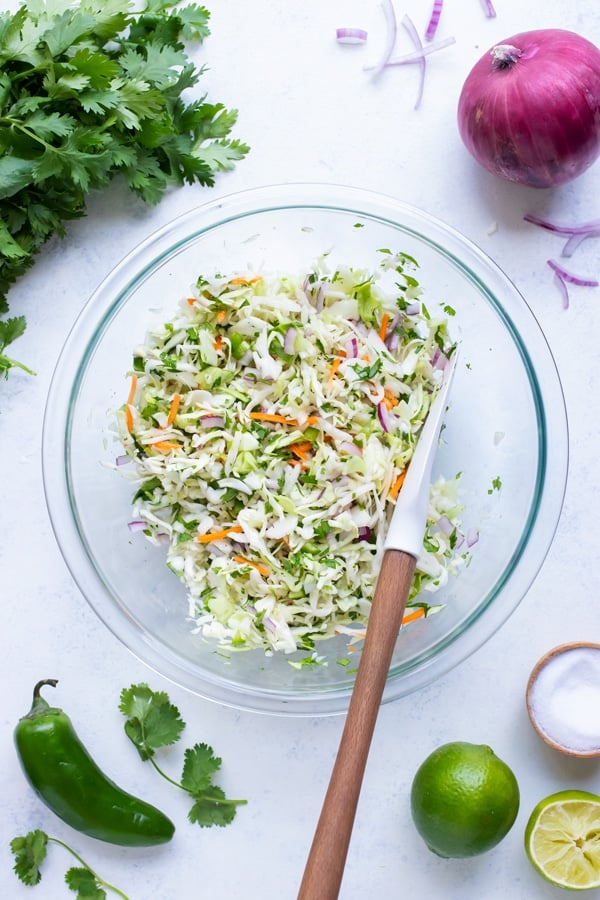 Taco slaw is made in a glass bowl and combined with a spatula.