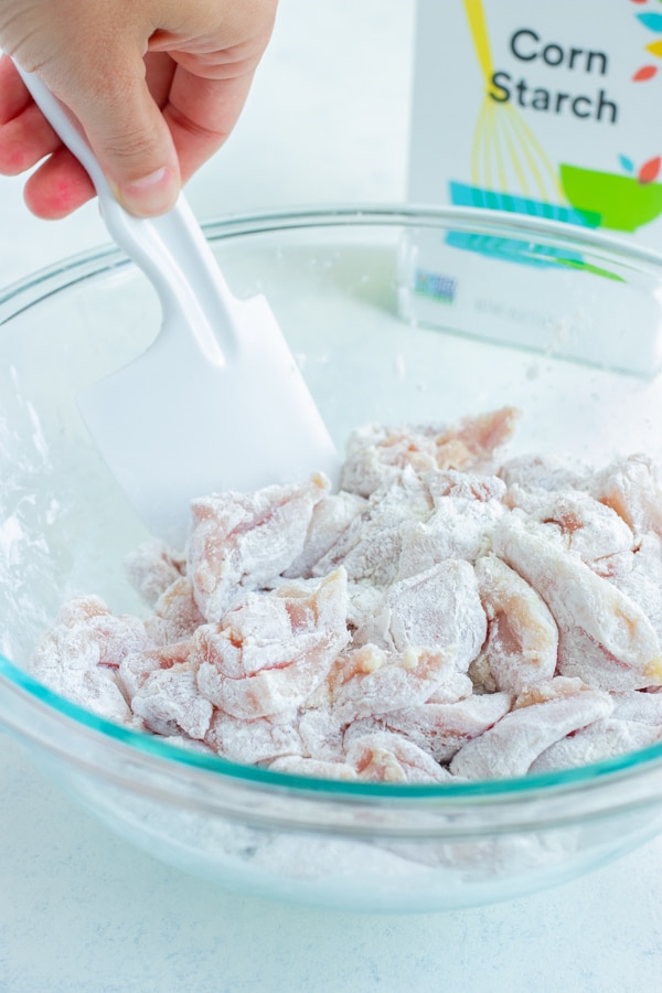 The raw chicken is coated in corn starch in a bowl.