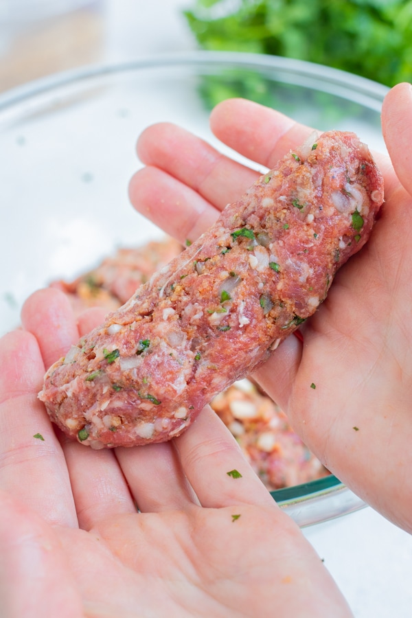 A hand is used to mold the lamb kofta into kebabs.