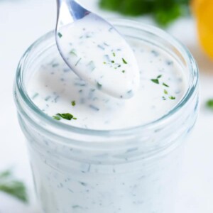 Ranch dressing is lifted out of a jar with a metal spoon.
