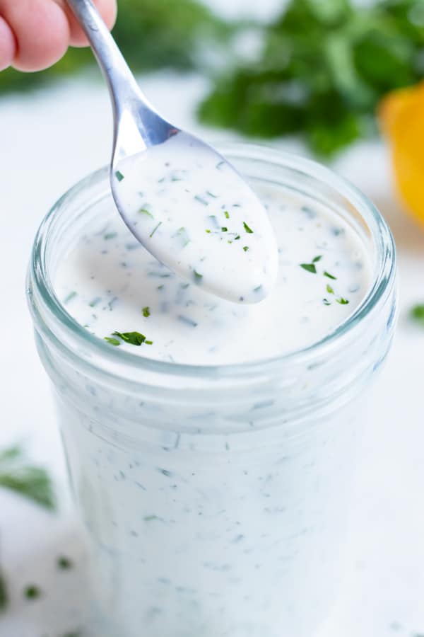 Ranch dressing is lifted out of a jar with a metal spoon.
