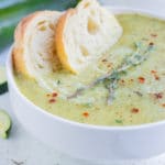 Creamy zucchini soup is served with bread in a bowl.