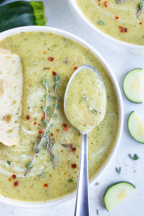 A metal spoon is used to eat this zucchini soup from a spoon.