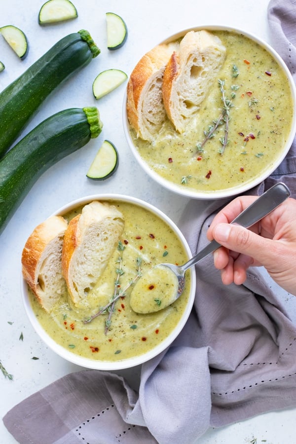 Two bowls of zucchini soup are set on the counter next to fresh zucchini.