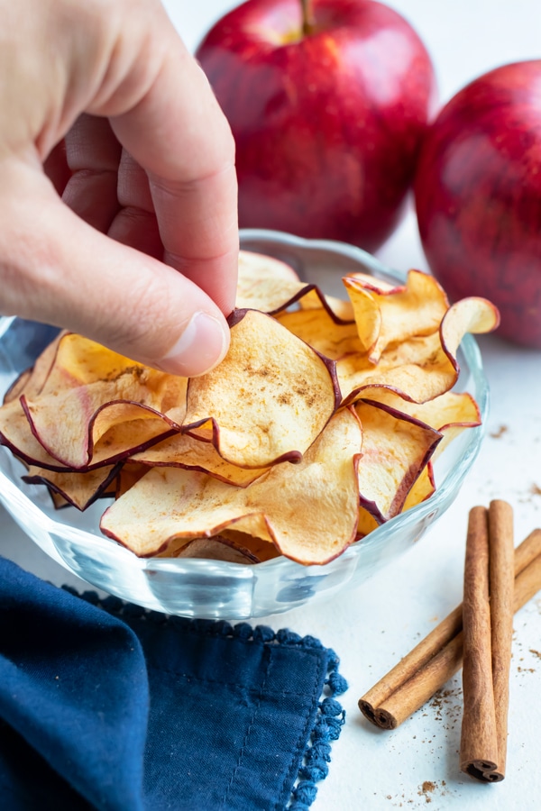 An apple chip is picked up by a hand for a snack.