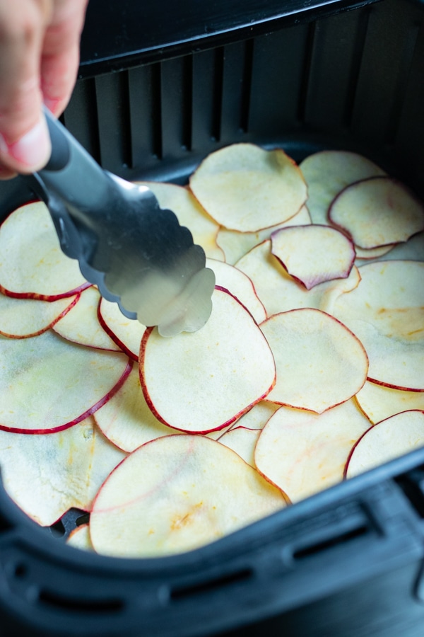 Tongs are used to flip the apple slices.