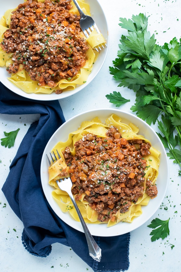 Two plates of beef bolognese sauce and pasta are shown on the counter.