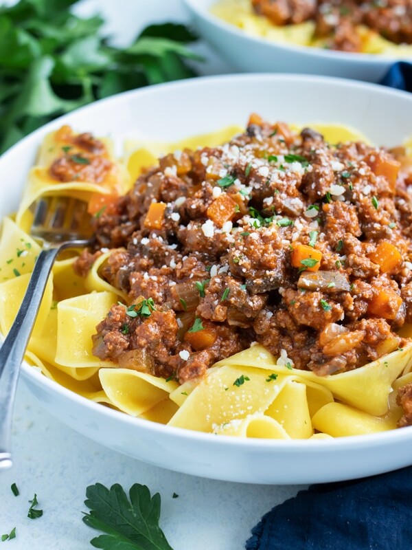 A bowl of bolognese sauce is topped with fresh grated Parmesan cheese.