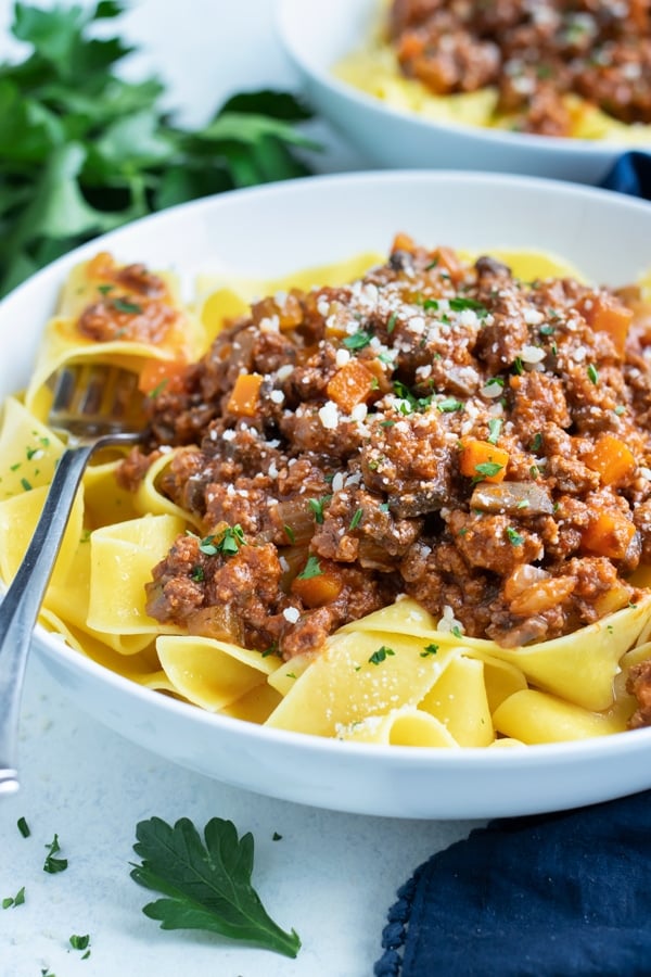 A bowl of bolognese sauce is topped with fresh grated Parmesan cheese.