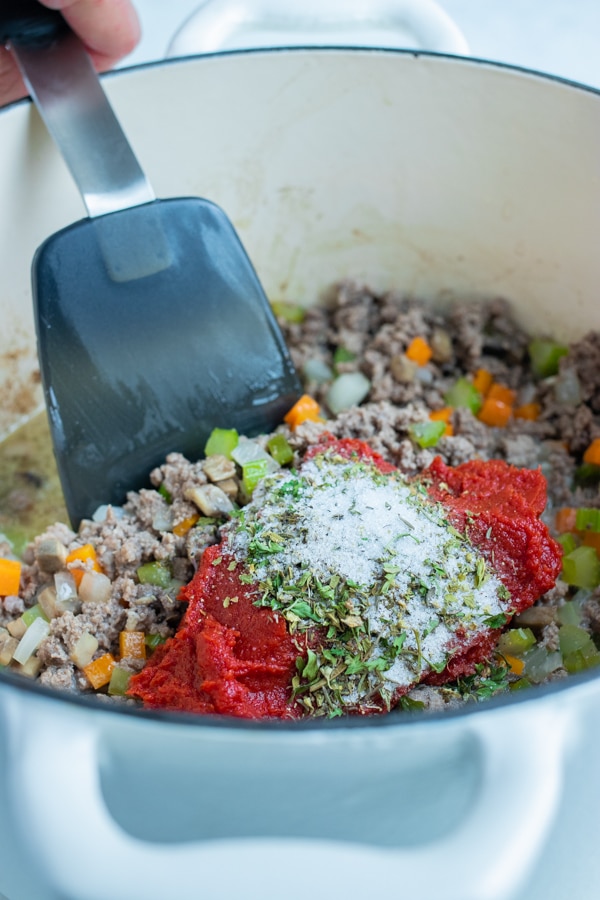 The seasonings and tomato paste are added to the ground beef and vegetables.