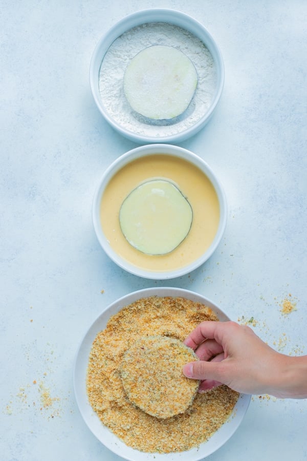 Eggplant slices are dipped in flour, egg, and breadcrumbs.