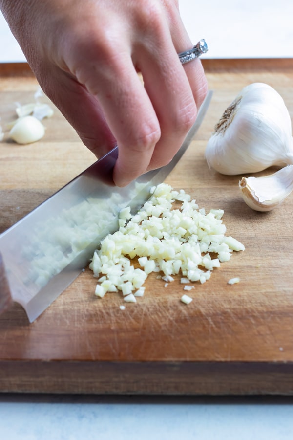 A knife is used to finely chop the garlic on cutting board.