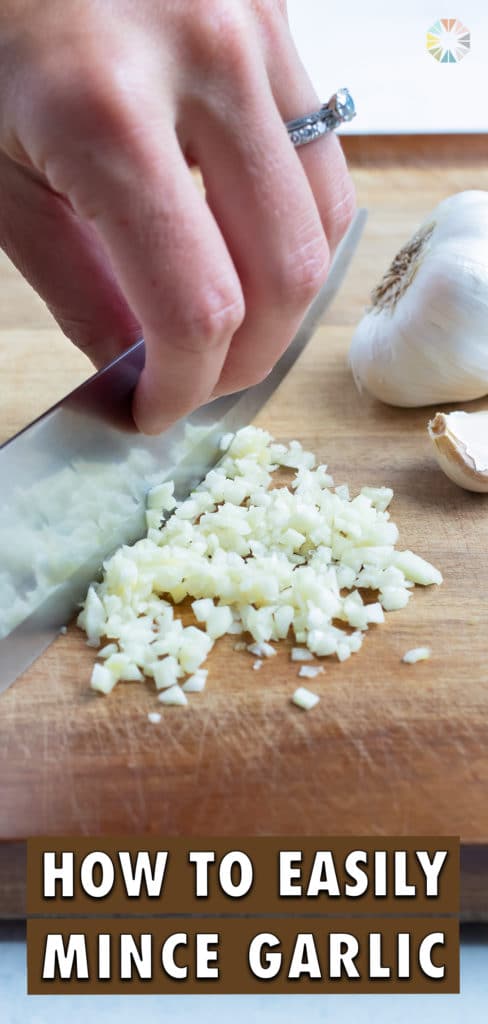 A knife is used to finely chop the garlic on cutting board.