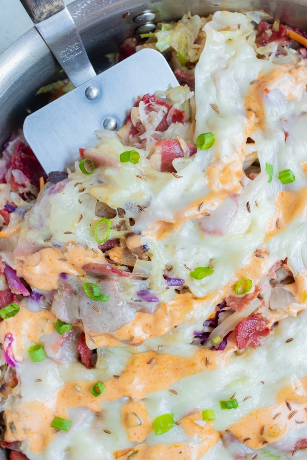 A metal spatula is used to dish this Reuben in a bowl.