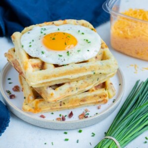 A plate is loaded with savory waffles, an egg, and syrup.