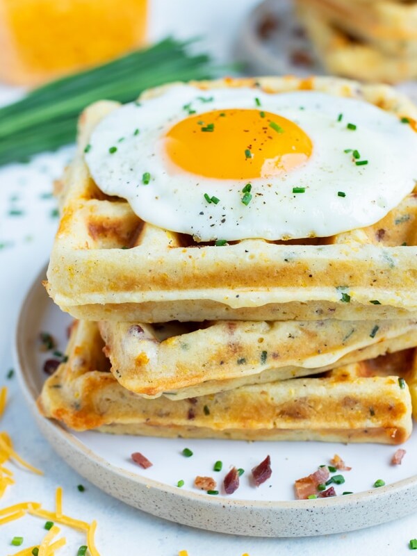 Savory waffles are stacked together on a plate for a filling breakfast recipe.
