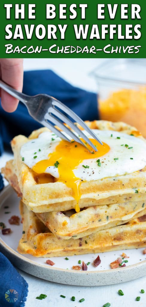 A fork is used to break open the egg on top of the waffles.
