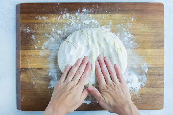 Hands covered in flour are used to press the gnocchi dough.