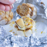 A spoon is used to remove a clove from the roasted garlic head.