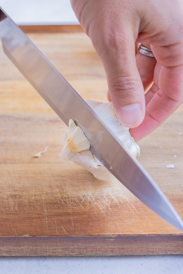 A knife is used to cut off the top of the head of garlic.