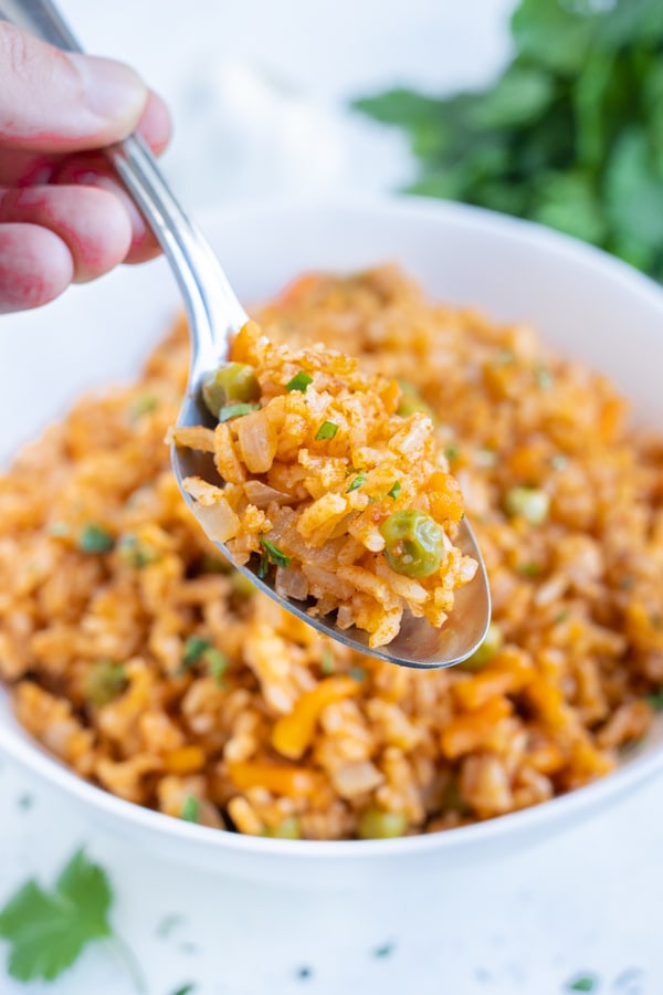 A spoon is full of fluffy and spicy Mexican rice from a bowl.