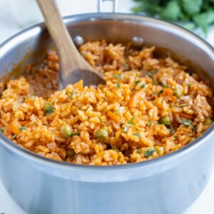 Homemade Mexican rice is dished with a wooden spoon from a pot.