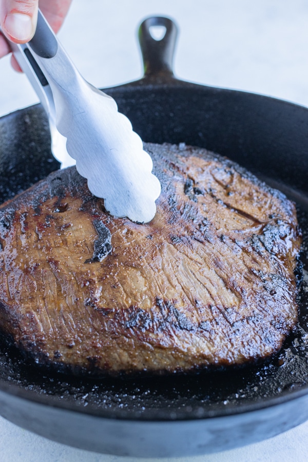 The marinated steak is cooked in a cast iron skillet.