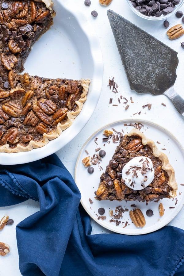 Chocolate pecan pie is shown on the counter next to a piece on a plate.