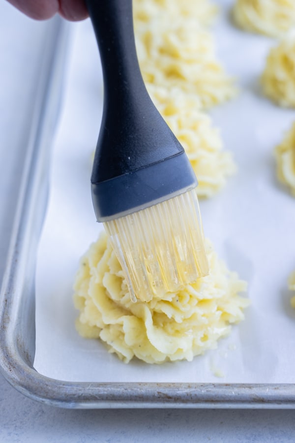 Duchess potatoes are brushed with butter.