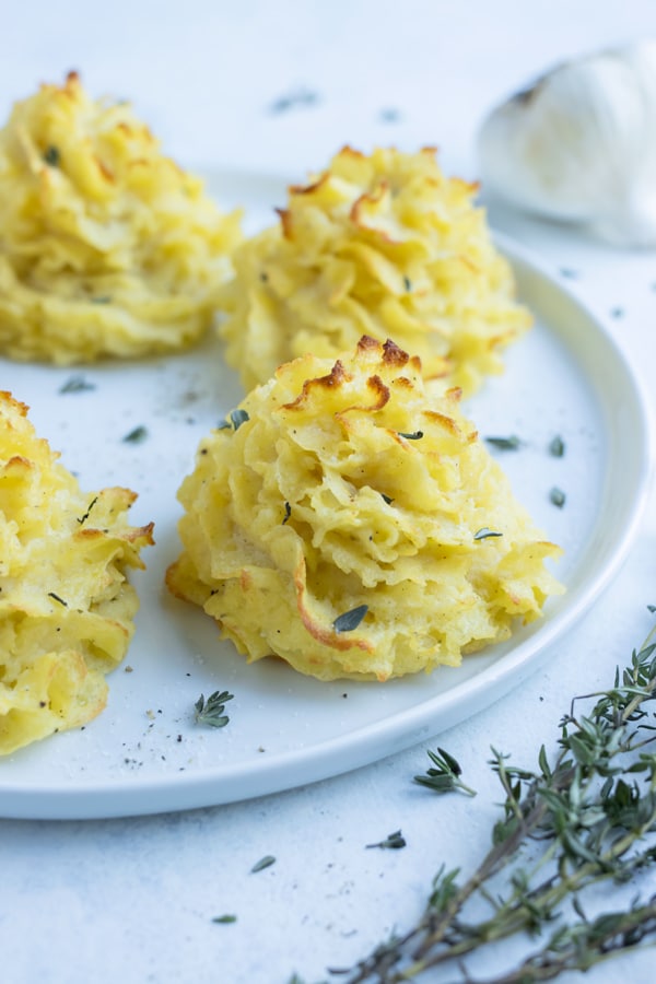 Golden and fluffy duchess potatoes are garnished with fresh herbs.