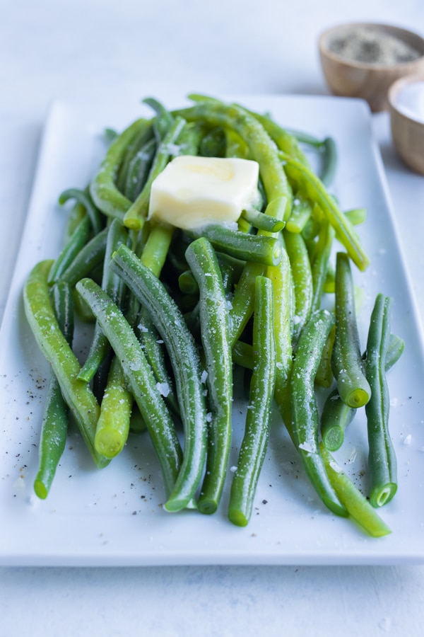 Blanched green beans are served on a plate with butter.