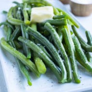 Boiled green beans shown on a plate with butter, salt, and pepper.