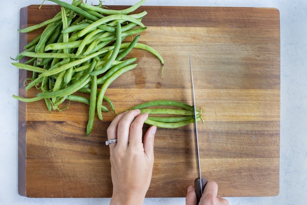 Multiple green beans are being trimmed to be boiled and blanched.