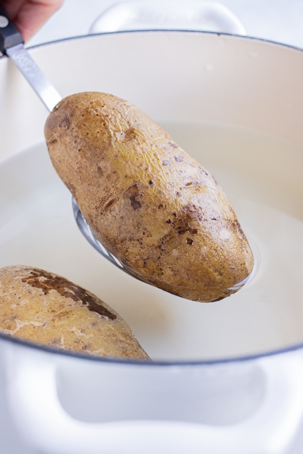A russet potato is lifted out of the boiling water.