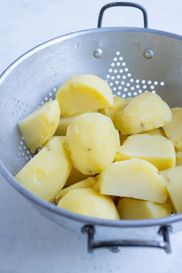 A colander is full of perfect boiled potatoes that have been peeled and cubed.