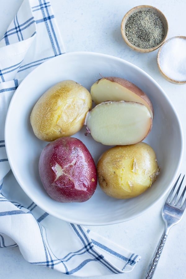 A white bowl is full of red potatoes, russet potatoes, and Yukon gold boiled potatoes.