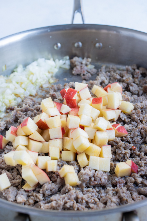 The diced apples are added to the sautéed sausage.