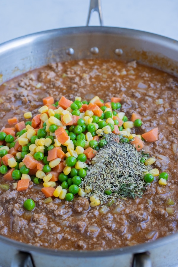 Seasonings and frozen vegetables are added to the pan.