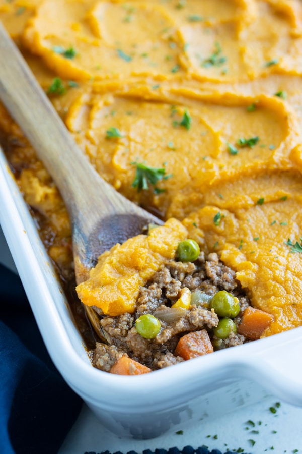 A serving of healthy sweet potato shepherd's pie is dished with a wooden spoon.