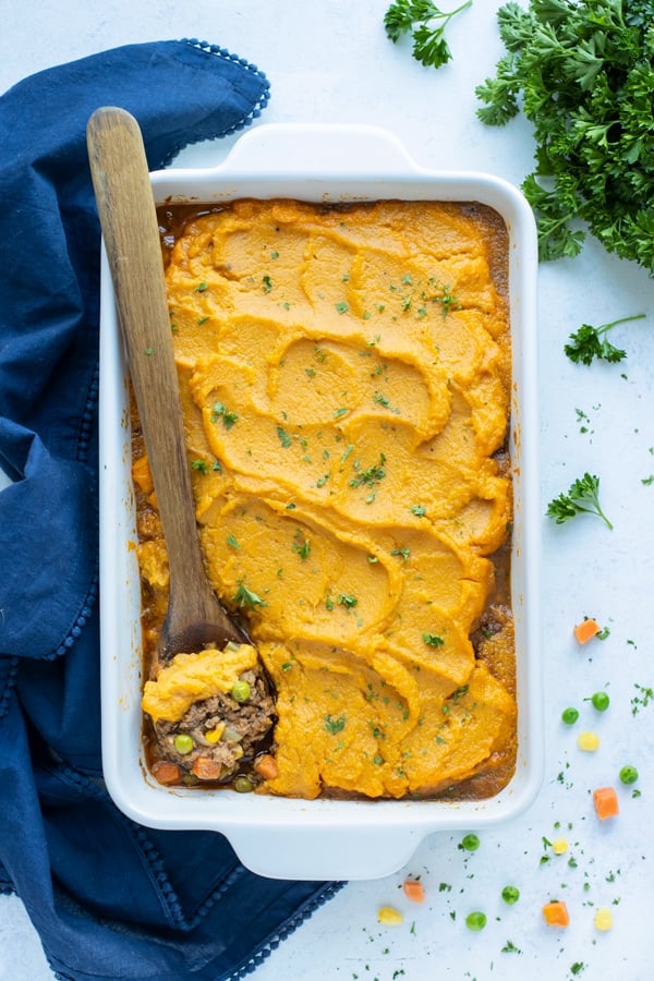 A wooden spoon is used to dish a serving of sweet potato shepherd's pie.