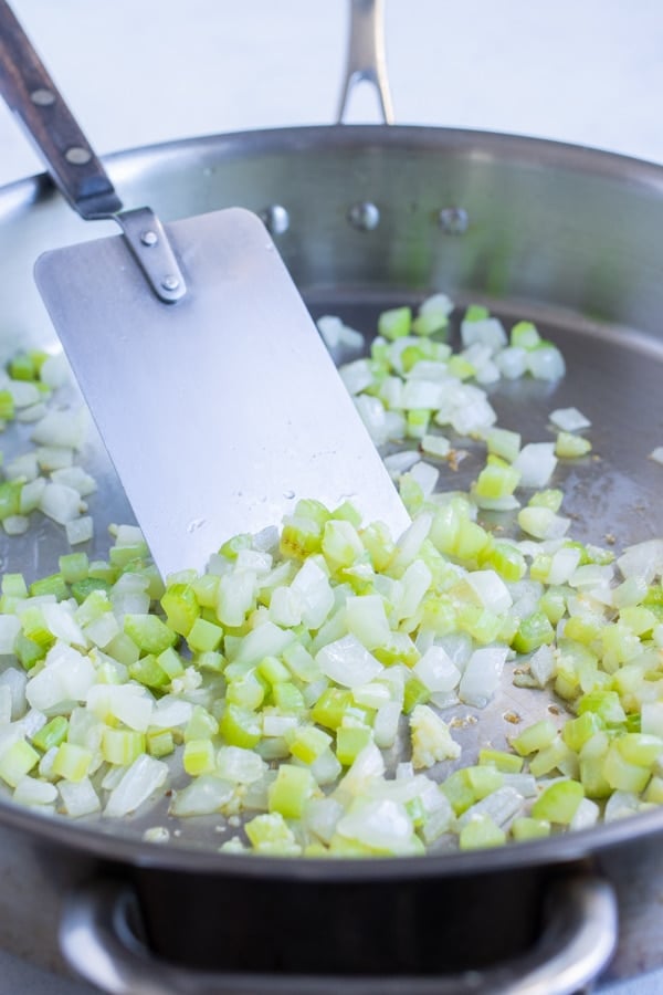 Diced onions and celery are sautéed on the stove.