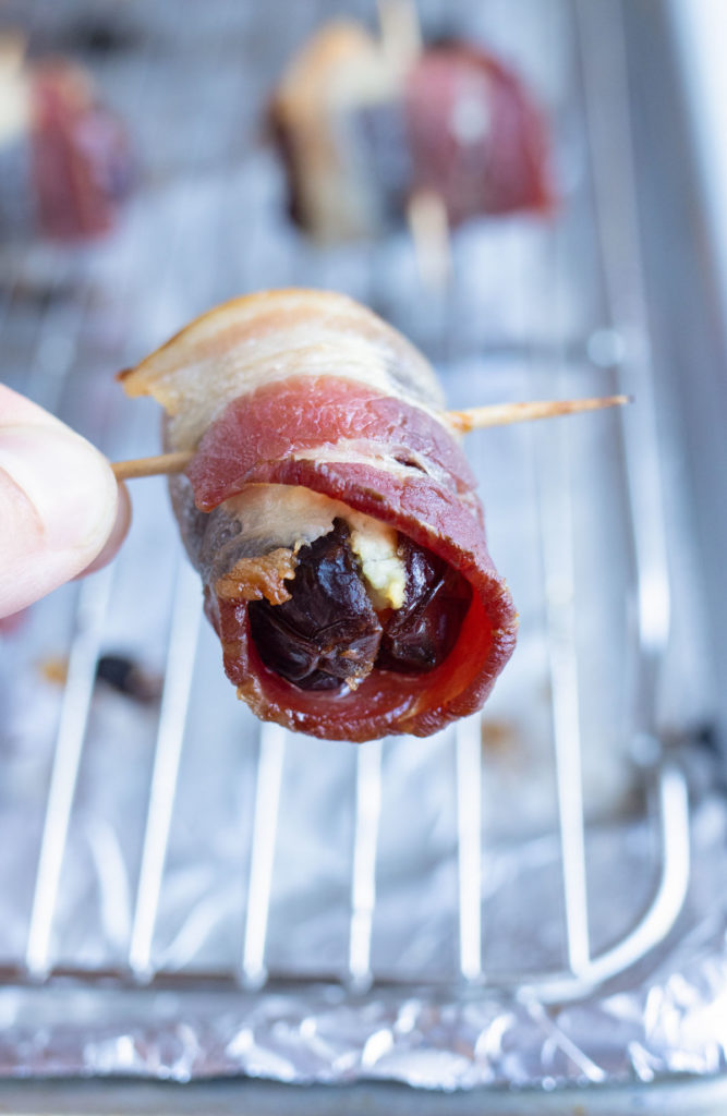 A date wrapped in bacon is lifted off the baking sheet.
