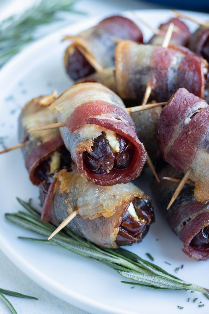 Bacon-wrapped dates are shown on a plate with fresh herbs.