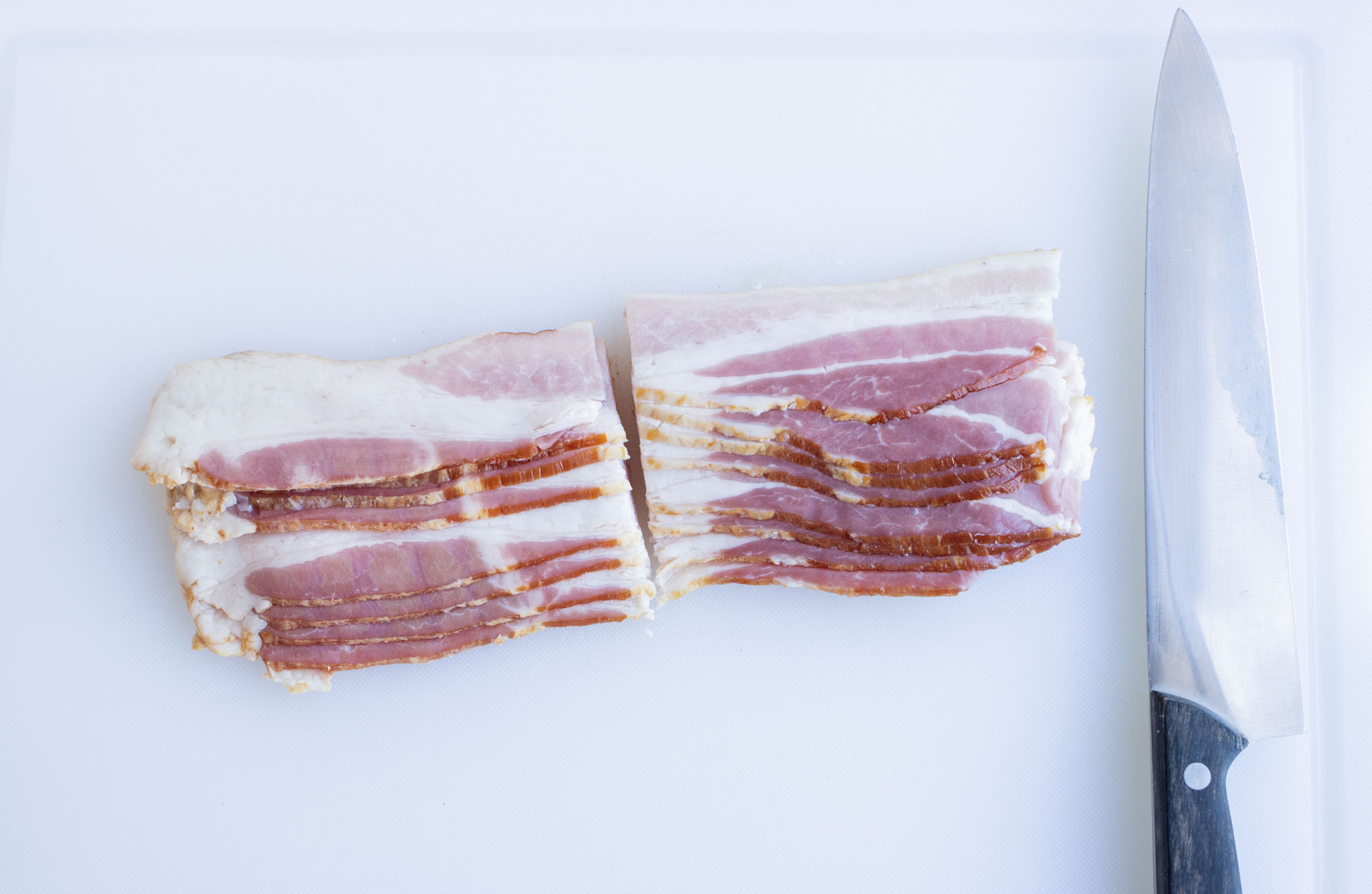 Bacon is cut in half on a cutting board.
