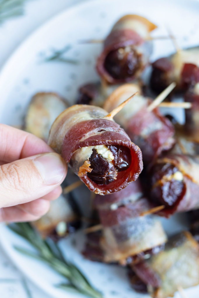 A bacon-wrapped date is picked up by a hand.