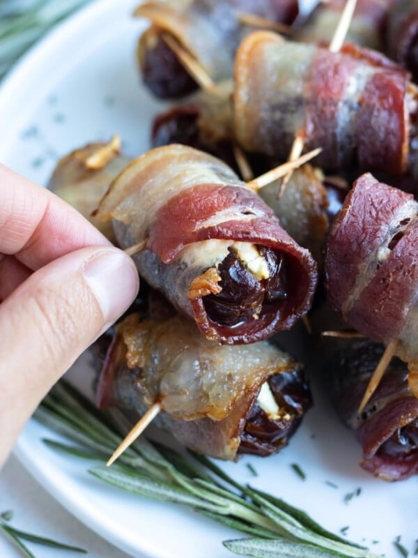 A hand is shown picking up a bacon wrapped date.