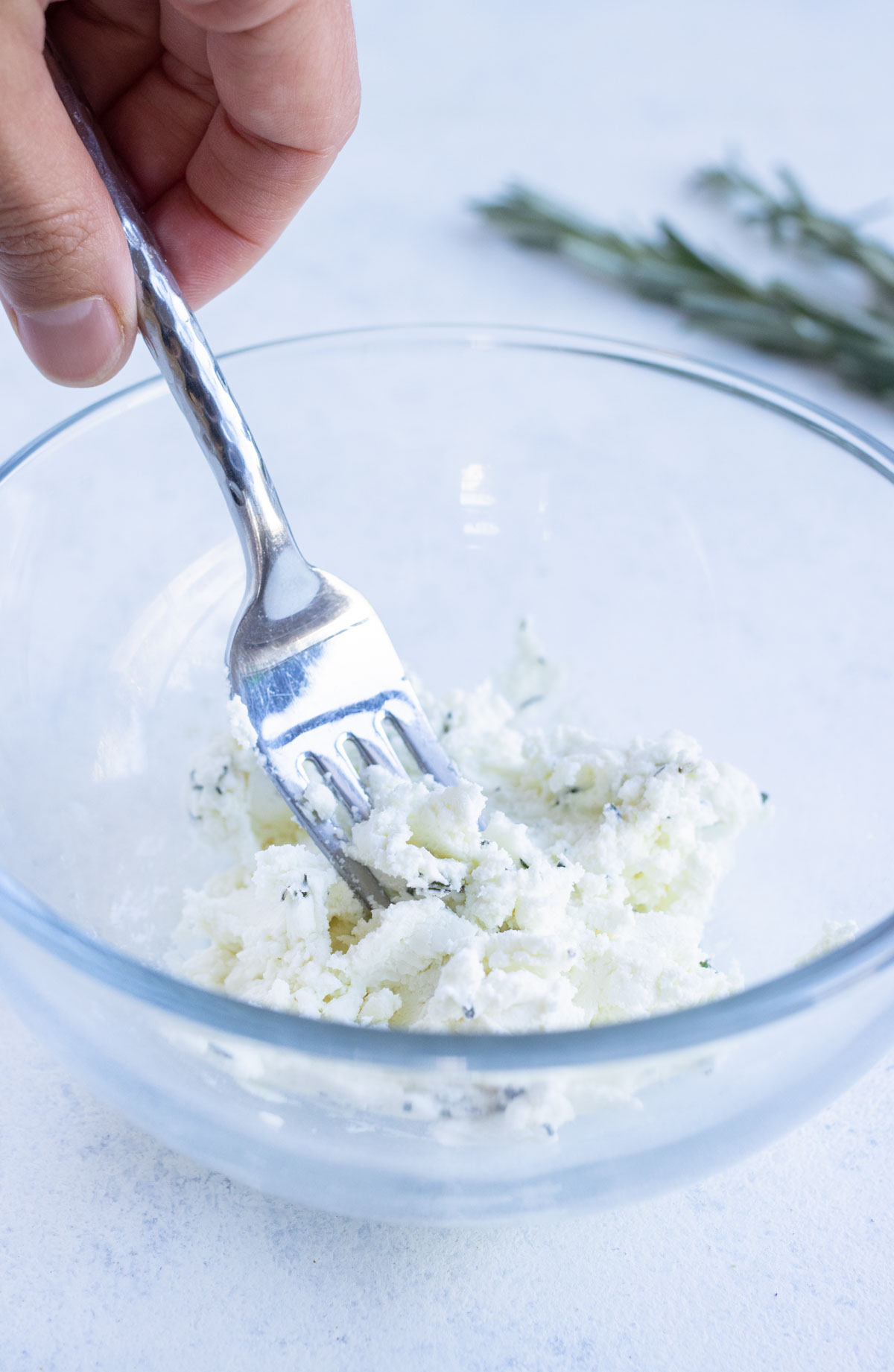Goat cheese, salt, and herbs are mixed in a bowl.