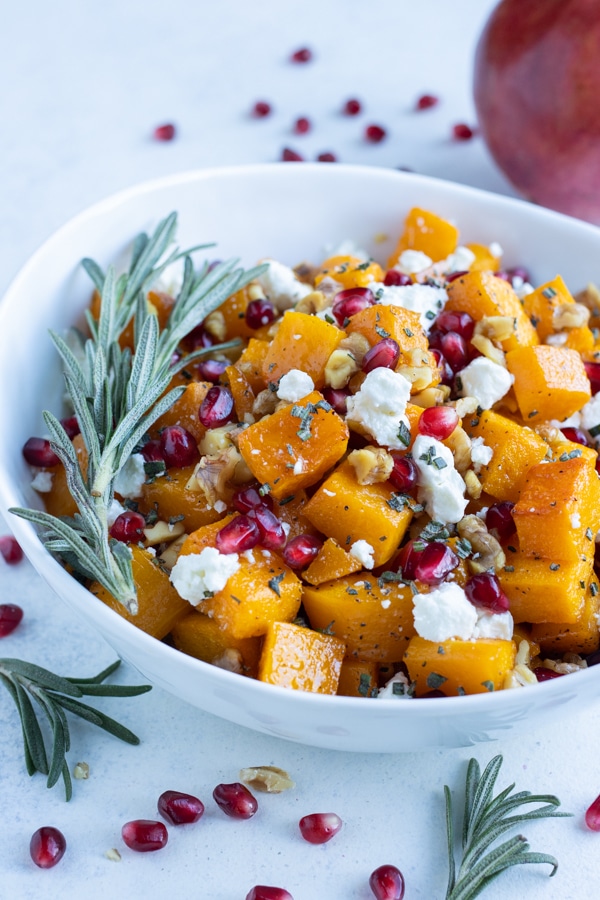 A white bowl is used to hold a batch of roasted butternut squash and goat cheese.